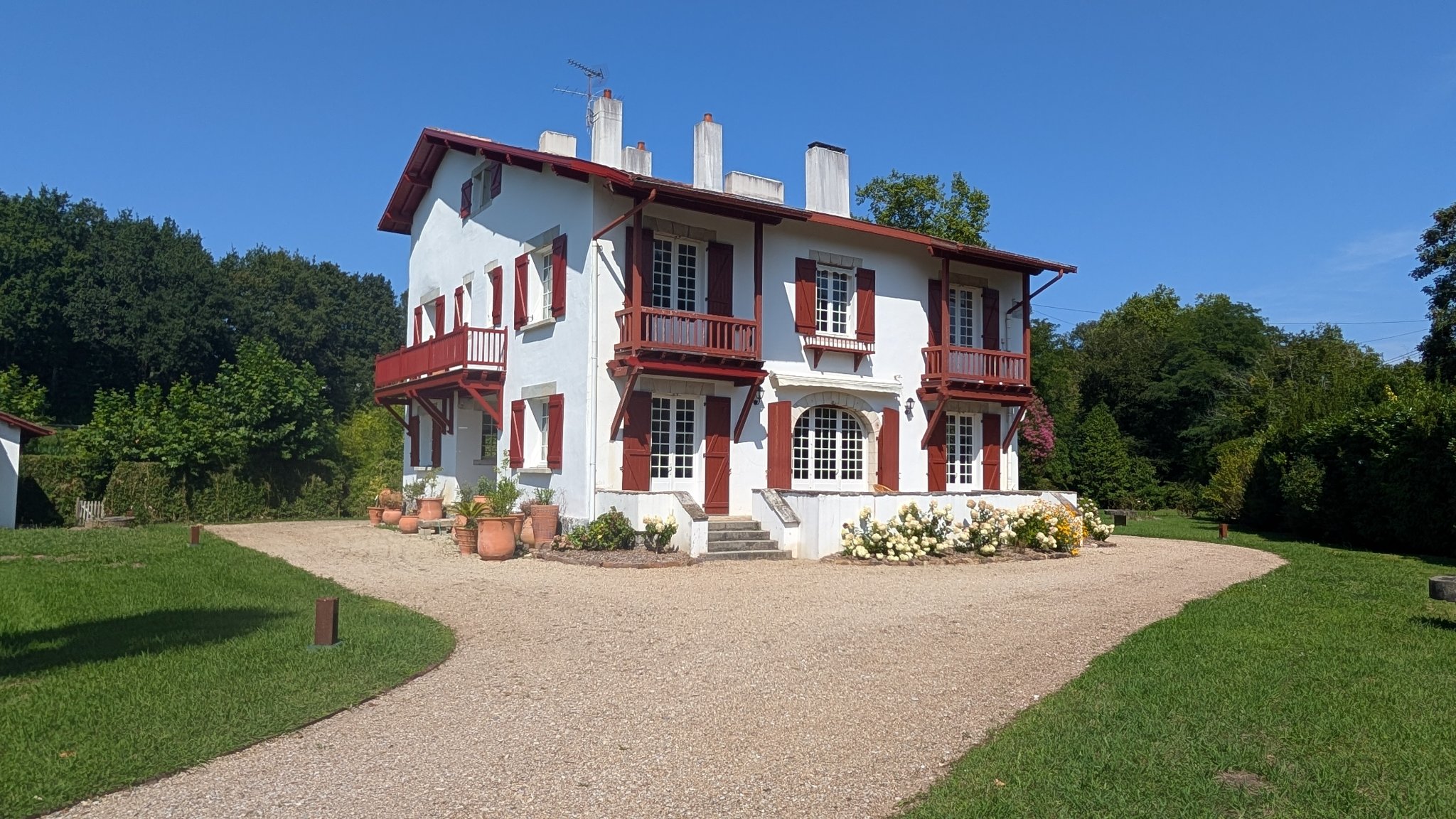 Allée de gravier et façade de la villa Harambidea avec ses volets rouges et son jardin